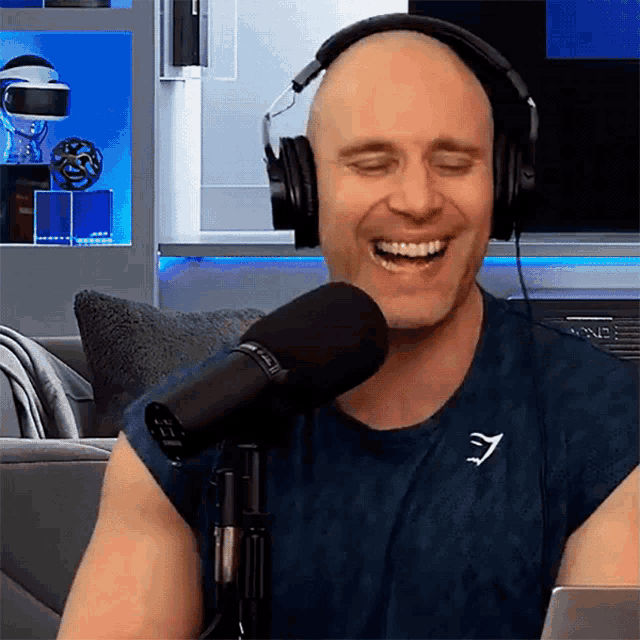 a bald man wearing headphones and a gymshark shirt is laughing into a microphone