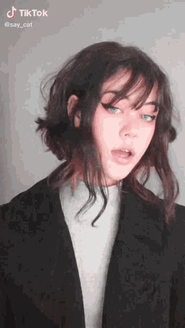 a woman with short hair is wearing a black jacket and a white sweater .