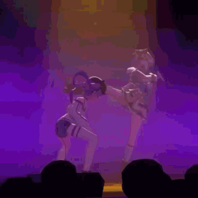 two anime girls are dancing on stage in front of a crowd .