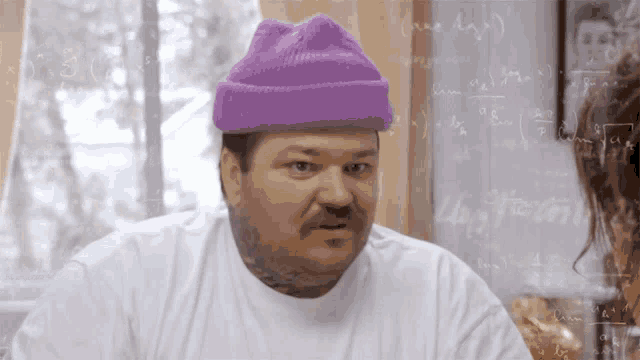 a man wearing a purple hat and a white shirt stands in front of a chalkboard with math equations on it