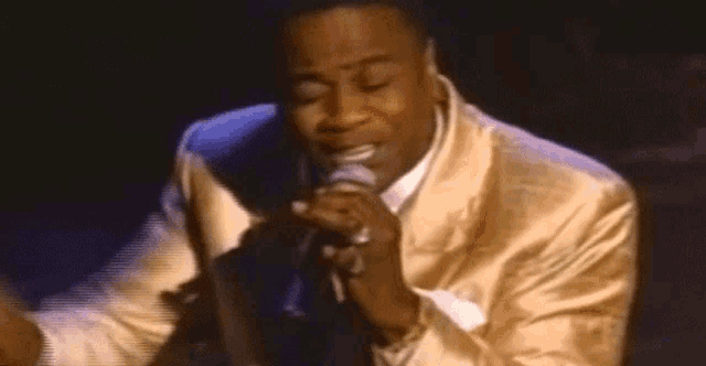 a man in a gold suit is singing into a microphone on stage