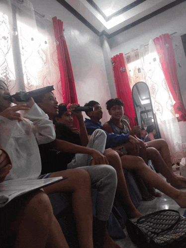 a group of people are sitting in a room with red curtains and a mirror