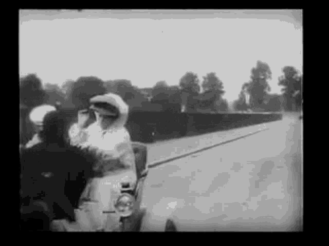 a black and white photo of a group of people riding in a car on a road .