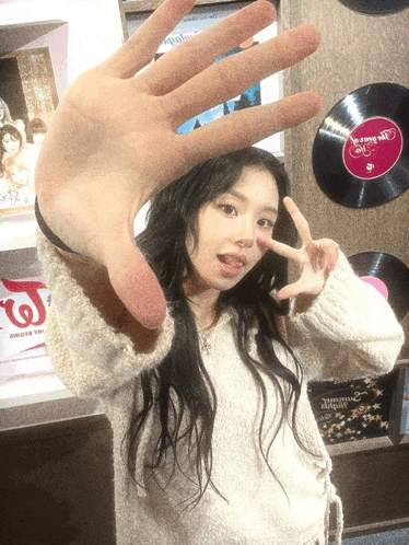 a woman making a peace sign with her hand in front of a wall with records on it