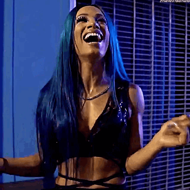 a woman with blue hair is laughing and wearing a black top .