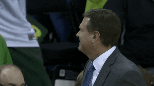 a man in a suit and tie laughs while sitting in the stands