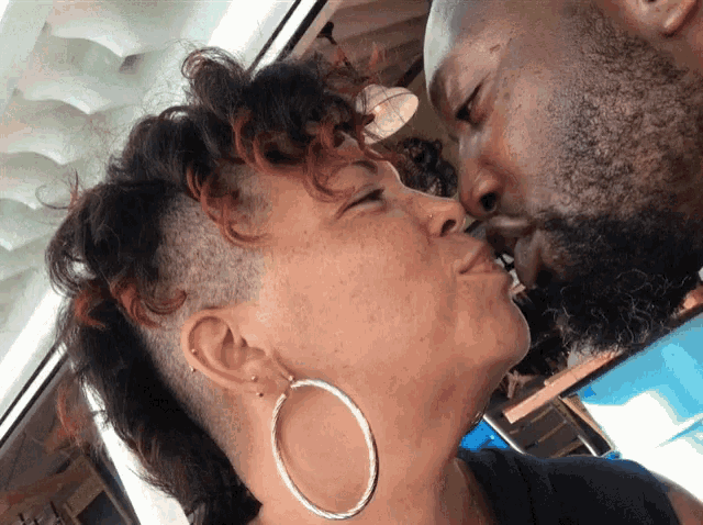 a woman wearing hoop earrings kisses a man on the forehead
