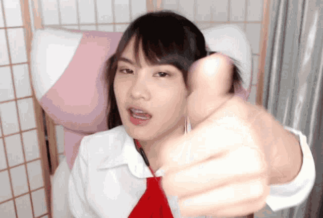 a girl in a white shirt and red tie giving a thumbs up