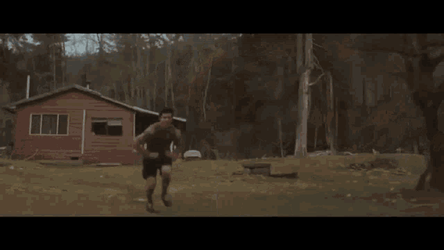a person is jumping in the air in front of a red house in the woods .