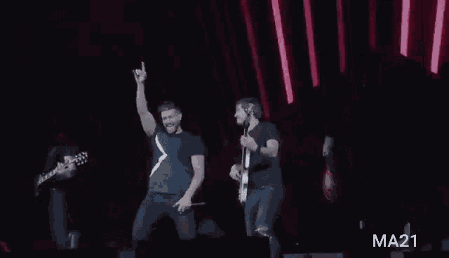 a group of men are standing on a stage playing guitars and singing into microphones .