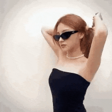 a woman wearing sunglasses and a pearl necklace is standing with her arms in the air .