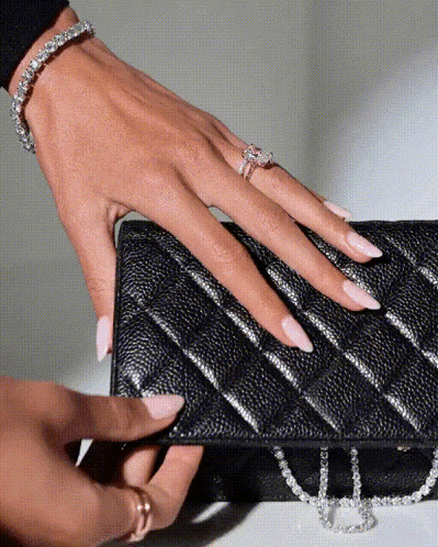 a woman 's hand with a diamond ring on it holds a black purse