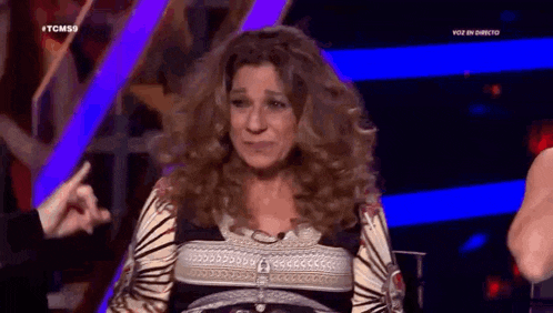 a woman with long curly hair is sitting on a stage talking to a man .