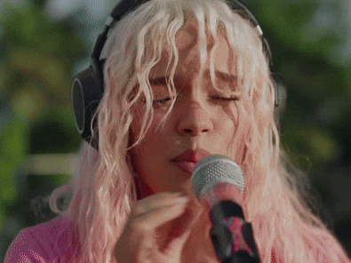 a woman with pink hair singing into a microphone