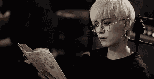 a woman wearing glasses is sitting in a chair reading a book .