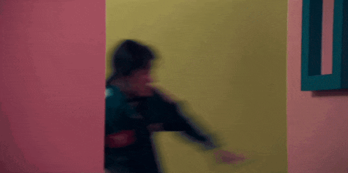 a blurry picture of a person standing in a room with a green jacket on .