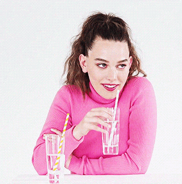 a woman in a pink sweater is drinking through a straw