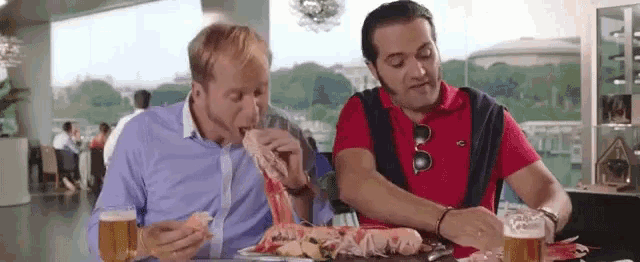 two men are sitting at a table eating and drinking