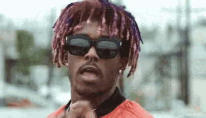 a man with purple hair and sunglasses is standing in front of a building .