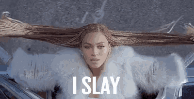 a woman with long braids is sitting in a car with her arms outstretched and her hair flying in the air .