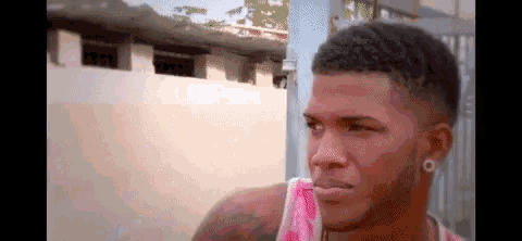 a close up of a man 's face with a pink tank top and earrings