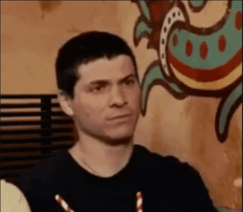 a man in a black shirt is sitting in front of a wall with a painting of a fish on it .