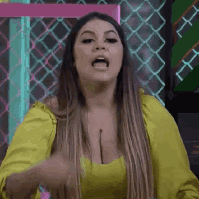 a woman in a yellow top is standing in front of a chain link fence and making a funny face .