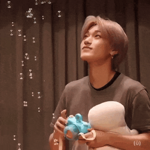 a young man is holding a stuffed animal and blowing bubbles