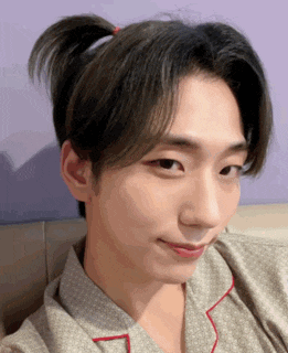a young man with his hair in a ponytail looks at the camera
