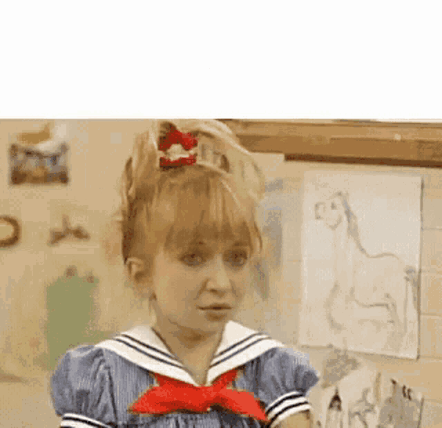a girl in a sailor dress with a red bow in her hair is standing in front of a wall with drawings on it .