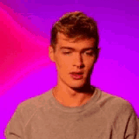 a young man in a grey sweater is standing in front of a purple and pink background .