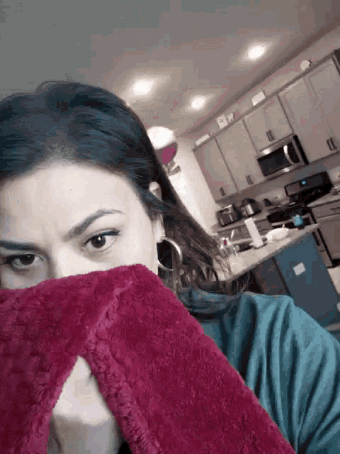a woman in a kitchen covering her face with a red blanket
