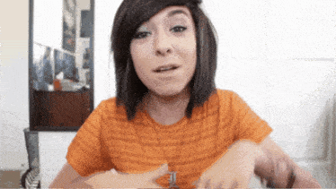 a woman wearing an orange striped shirt has a necklace with the letter i on it