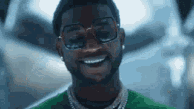 a young man wearing glasses and a green shirt is smiling .