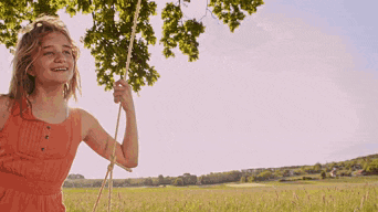 a young girl in an orange dress is swinging on a rope in a field
