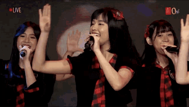 a group of girls singing in front of a screen that says live