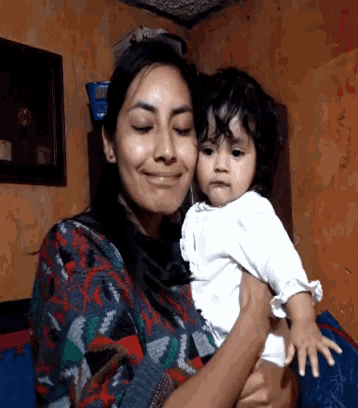 a woman holds a baby in her arms and smiles at the camera