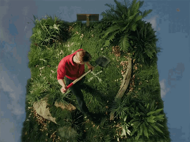 a man in a red shirt is digging in the grass