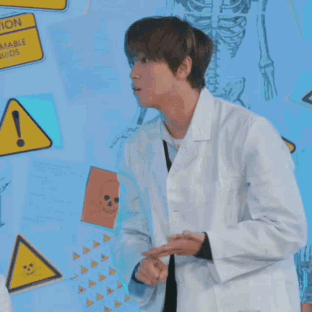 two men in lab coats are sitting at a table in front of a wall that has a caution sign on it