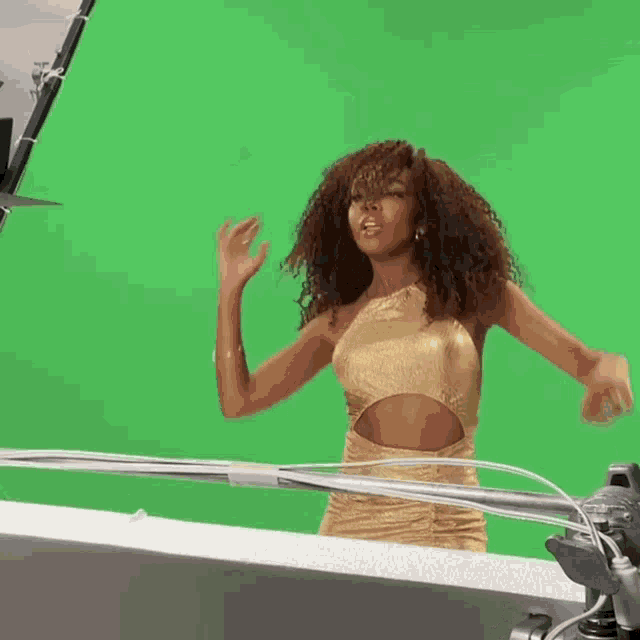 a woman in a gold dress stands in front of a green background