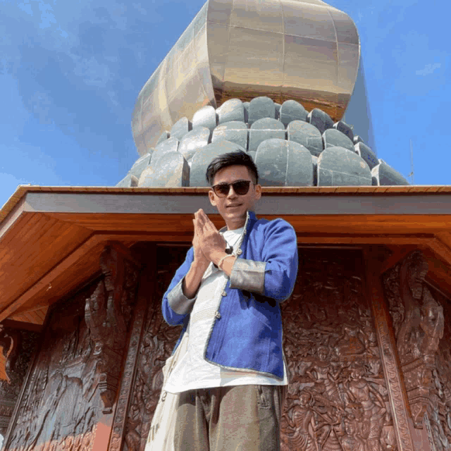 a man wearing sunglasses and a blue jacket stands in front of a large statue