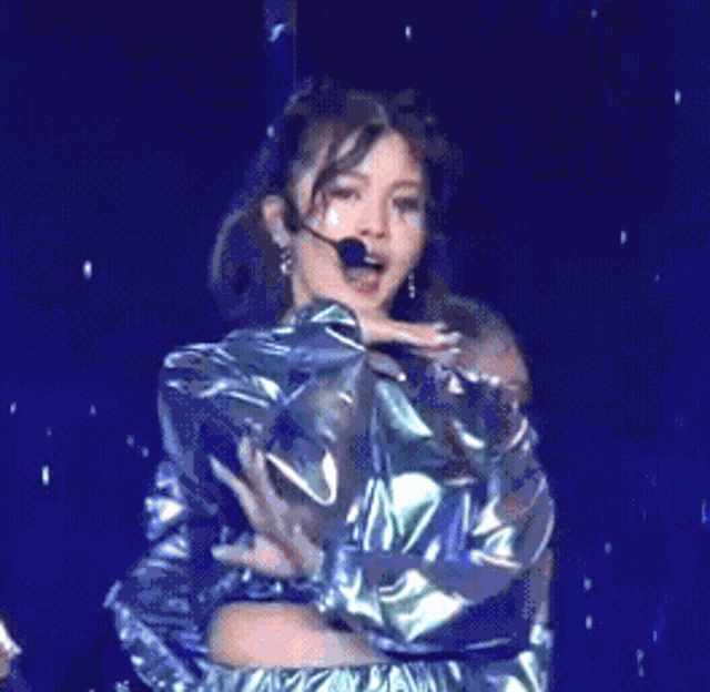 a woman wearing a microphone and a metallic jacket is dancing on a stage