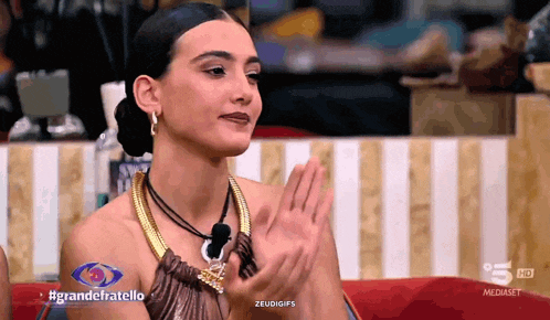 a woman clapping in front of a sign that says grandefratello on it