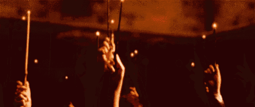 a group of people are holding up their wands in the air in a dark room .