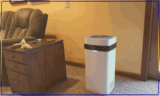 a white air purifier is sitting in a living room next to a couch and desk
