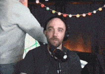 a man wearing headphones sitting in front of a microphone with a string of lights hanging from the ceiling behind him