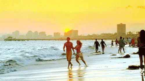 a man and a woman are dancing on a beach with the sun setting behind them