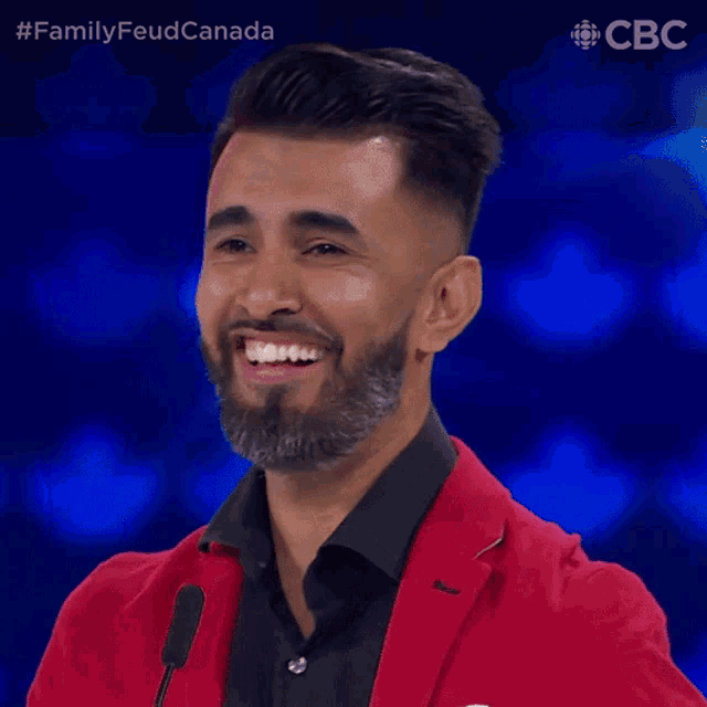a man with a beard wearing a red jacket and black shirt is smiling in front of a cbs logo
