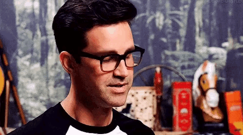a man wearing glasses and a black shirt is smiling and looking to the side .