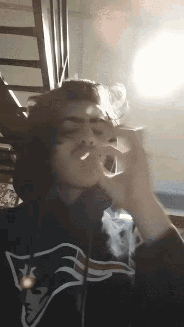 a man wearing a patriots sweatshirt smoking a cigarette